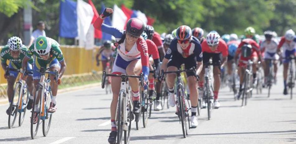 Paola Andrea Muñoz aprieta su puño al momento de cruzar la meta en la primera posición en la celebración del Campeonato Panamericano de Ciclismo. Detrás figura el pelotón.