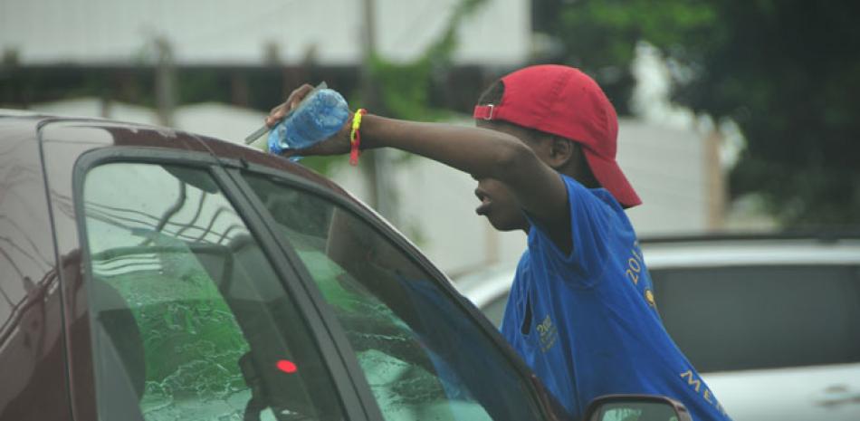 Las calles. Este adolescente usa una botella plástica con agua sobre el parabrisas de un vehículo, buscando pago por este servicio.