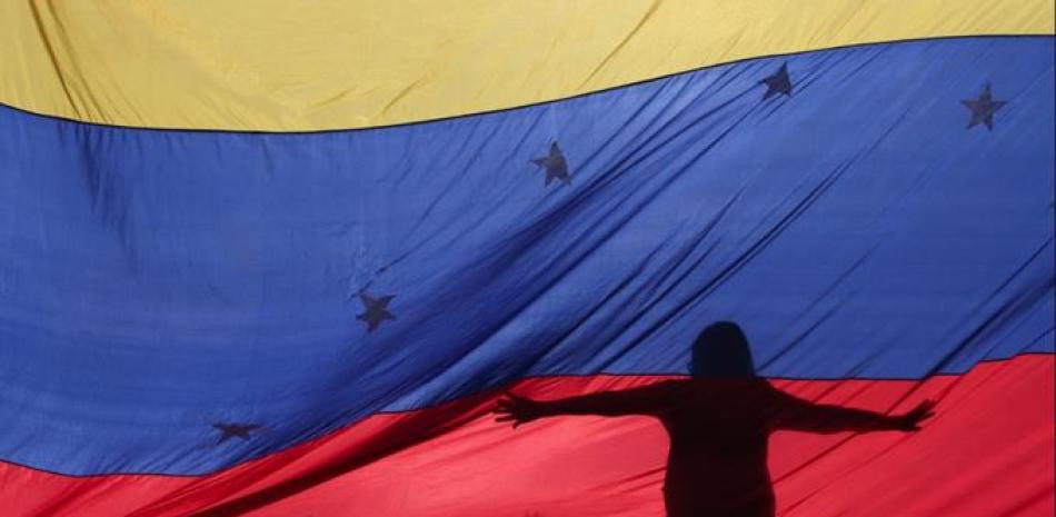 Fotografía de archivo del 10 de julio de 2017 de siluetas de manifestantes antigubernamentales a través de una bandera venezolana durante una manifestación convocada por la oposición en Caracas. (AP Foto/Fernando Llano, Archivo)