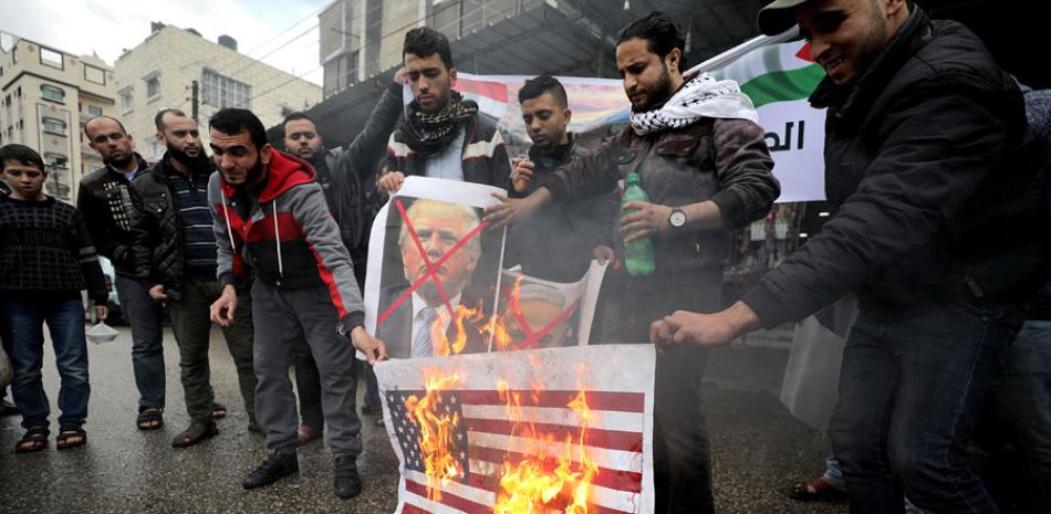 Protestas. Varios palestinos queman una bandera estadounidense y de Israel, e imágenes del presidente de EE.UU., Donald Trump, y del primer ministro israelí Benjamin Netanyahu, durante una protesta ayer en Rafah, Cisjordania.