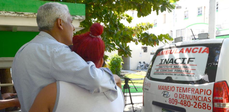 Dos familiares observan el vehículo del Instituto Nacional de Ciencias Forenses donde trasladan el cadáver de su pariente, otra víctima de los frecuentes feminicidios que preocupan a la sociedad dominicana.
