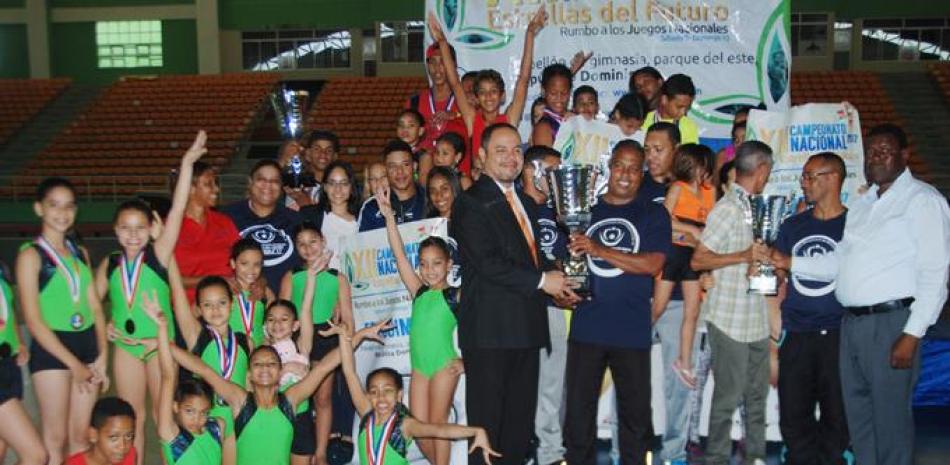 Edwin Rodríguez, presidente de la Federación Dominicana de Gimnasia, entrega el trofeo de campeón al entrenador de Santiago, Juan Lamour. Figuran Fernando Whyte, secretario general de la Fedogim, así como atletas de Santiago.