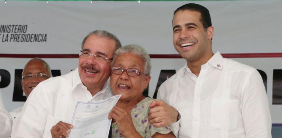 Acto. El presidente Danilo Medina entrega título definitivo a una beneficiaria, junto al director de la Comisión Permanente de Titulación de Terrenos del Estado, José Dantés.