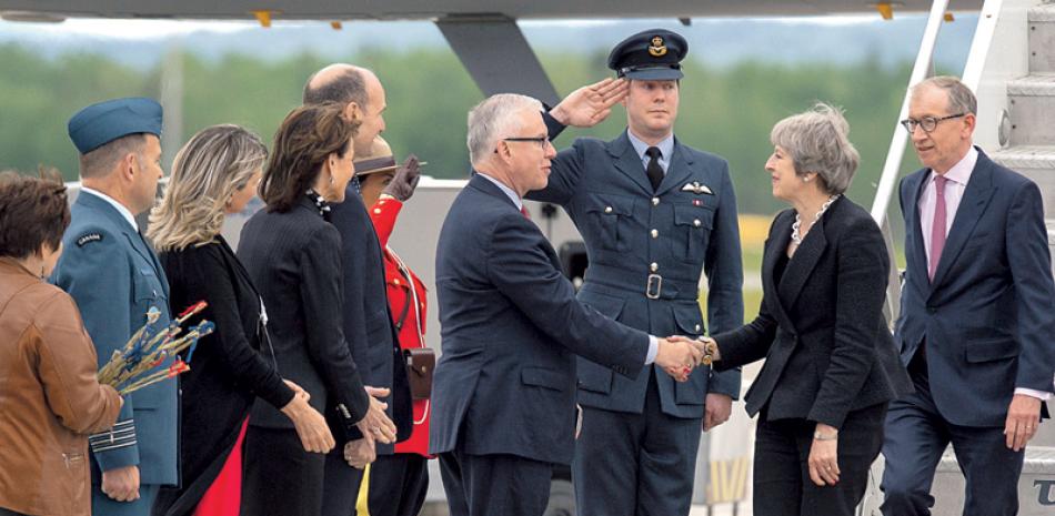 Bienvenida. La primera ministro británica, Theresa May, y su esposo, Philip May, a la derecha, son recibidos por el jefe de Protocolo canadiense, Roy Norton, tras llegar al aeropuerto en CFB Bagotville, en Quebec.