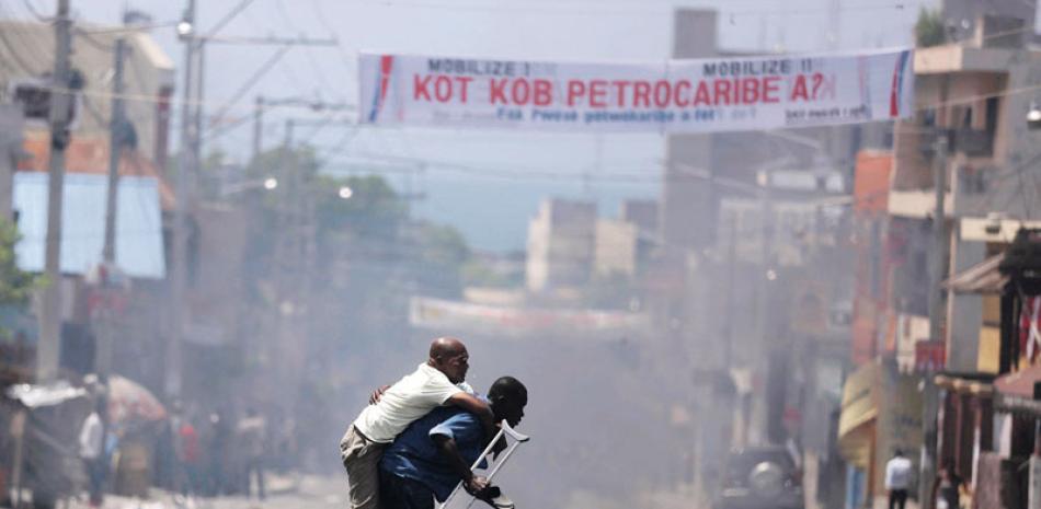 Ayuda. Un discapacitado es cargado a través de una calle inundada por el humo de las bombas lacrimógenes, durante una manifestación contra el mal uso de los fondos de Petrocaribe, por la administración actual y pasadas, en Puerto Príncipe, el 9 de septiembre pasado.