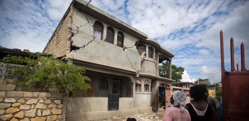 Tragedia. Un grupo de personas mira un edificio dañado por el movimiento telúrico de 5,9 grados ocurrido durante la noche del pasado sábado en Gros Morne, Haití.