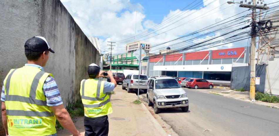 Acción en curso. Un oficial del Intrant toma fotos de vehículos en marcha y de otros estacionados en una vía del ensanche Miraflores.
