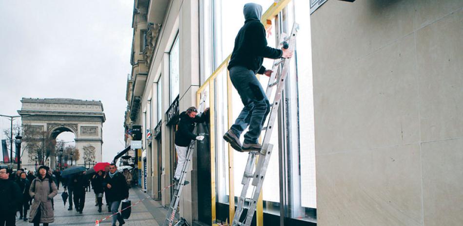 Protección. Trabajadores colocan protección en las ventanas de exhibición de una tienda en la avenida de los Campos Elíseos en la capital francesa. Los dueños de tienda están listos para enfrentar la violencia, levantando paredes con cartón piedra, por las protestas de hoy sábado.