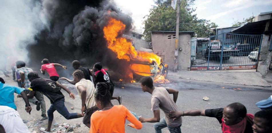 Manifestación. Los manifestantes huían ayer de la policía que está disparando en su dirección, mientras un automóvil se quema durante una protesta que exige la renuncia del presidente haitiano, Jovenel Moïse, en Puerto Príncipe, Haití.
