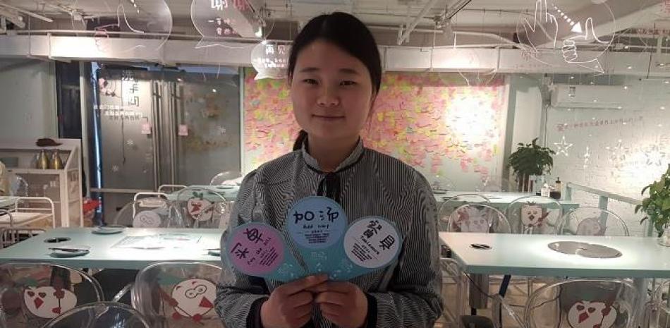 La camarera Cao Xueting, del restaurante 'Forgive Barbecue' de Pekín, sostiene las "cartas-guía" con las que puede comunicarse con los clientes, pese a su discapacidad auditiva. EFE/Javier Castro Bugarín