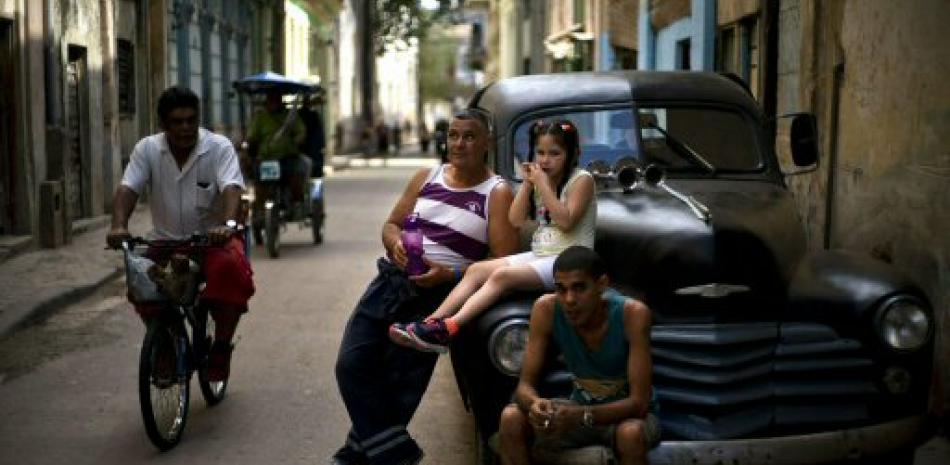 Cubanos descansan en un automóvil estadounidense clásico mientras un hombre pedalea su bicicleta en La Habana. Foto: AP