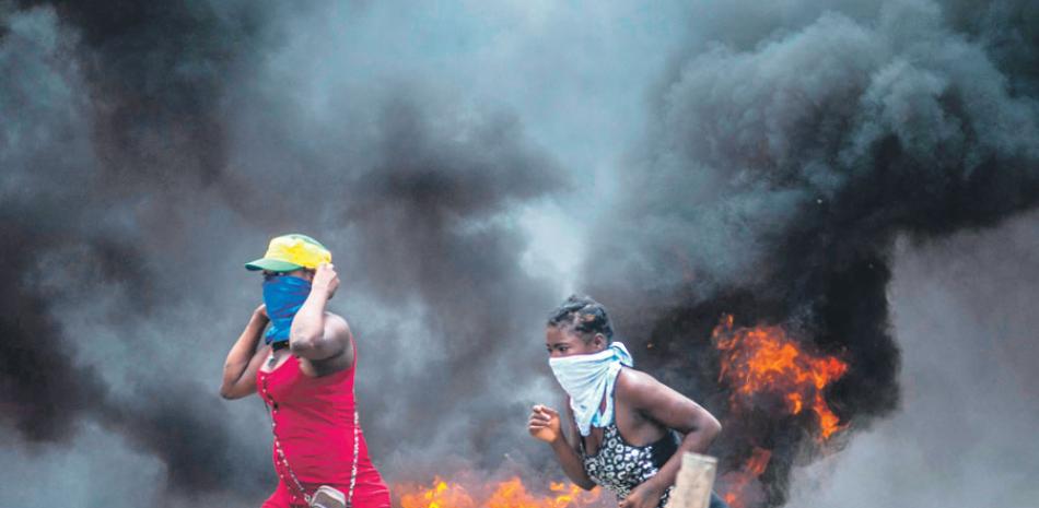Dos mujeres con el rostro cubierto pasan frente a una barricada en llamas ayer lunes, en Puerto Príncipe. EFE