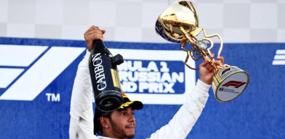 Lewis Hamilton sostiene una botella de champagne en una mano y el trofeo de campeón en la otra tars ganar el GP de Rusia.
