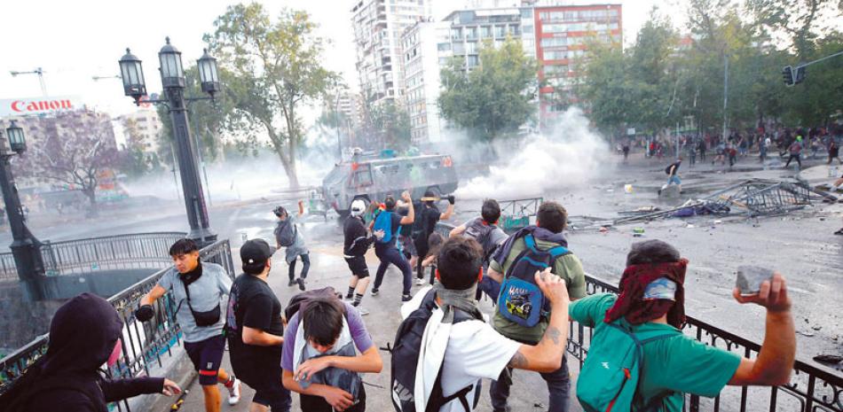 Jóvenes chilenos lanzan piedras contra un vehículo armado del gobierno chileno. EFE