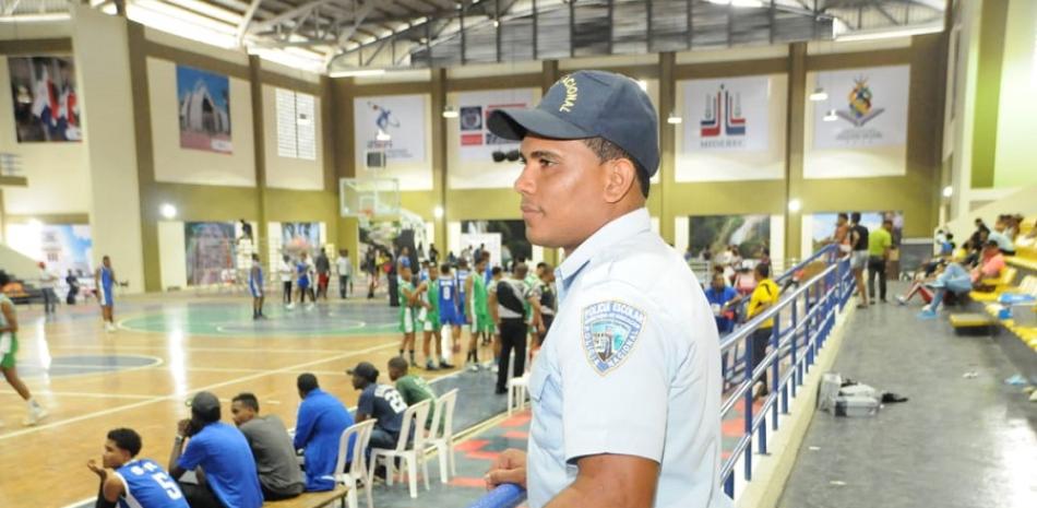Un miembro de la policía de la Policía Escolar contempla desde el pasillo del polideportivo de Monte Plata una competencia de los Juegos Nacionales.
