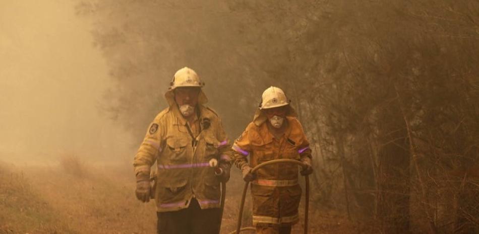 Dos bomberos arrastran una manguera de agua tras apagar un incendio cerca de Moruya, Australia, el 4 de enero de 2020. (AP Foto/Rick Rycroft)