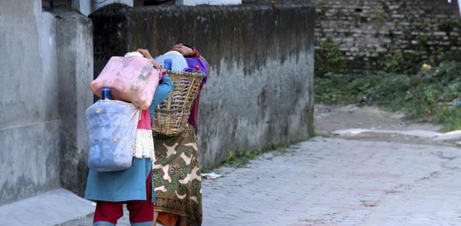 Dos mujeres cargan botellas y frascos de agua de un grifo tradicional conocido como Rani Devi Dhunge Dhara hasta sus casas en Katmandú, Nepal. (Purnima Shrestha/The New York Times)
