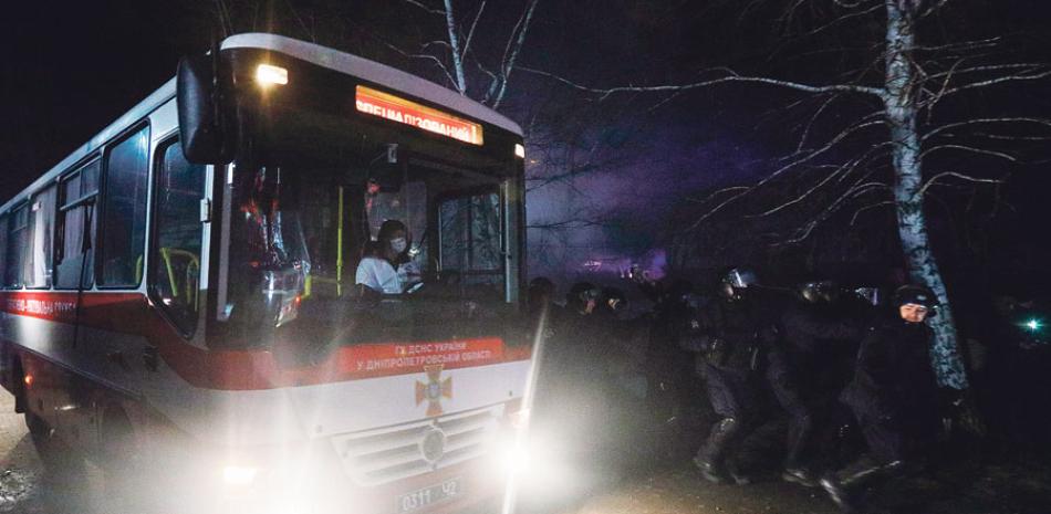 La policía antimotines corre para hacer retroceder a manifestantes que planean detener a los autobuses que trasladan a pasajeros que fueron desalojados de la ciudad china de Wuhan, en Novi Sarzhany, Ucrania. AFP