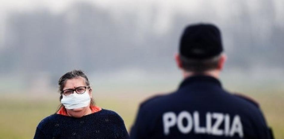 Un residente que usa una máscara respiratoria habla con un oficial de policía que brinda información en la entrada de la pequeña ciudad de Casalpusterlengo, al sureste de Milán, a la sombra de un nuevo brote de coronavirus. Miguel Medina/AFP.