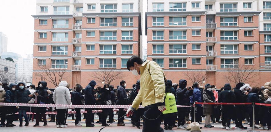 Un funcionario del gobierno rocía desinfectante como medida de precaución contra el Covid-19 cerca de gente que hace fila para comprar mascarilla, en el exterior de una tienda, en Seúl, Corea del Sur. AP