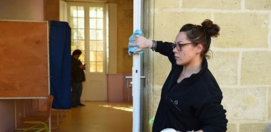 Una mujer desinfecta la puerta de un colegio electoral en Burdeos, suroeste de Francia, durante la primera vuelta de las elecciones a la alcaldía en Francia, mientras este país lucha contra el coronavirus que causa la enfermedad COVID-19. Nicolas Tucat/AFP.