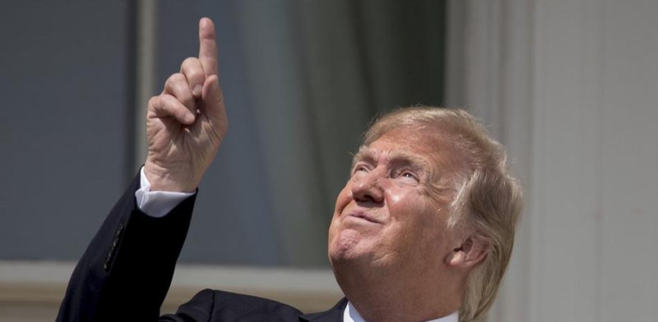 Fotografía de archivo del 21 de agosto de 2017, del presidente Donald Trump apuntando al sol durante un eclipse solar fuera de la Casa Blanca, en Washington. (AP Foto/Andrew Harnik, Archivo)