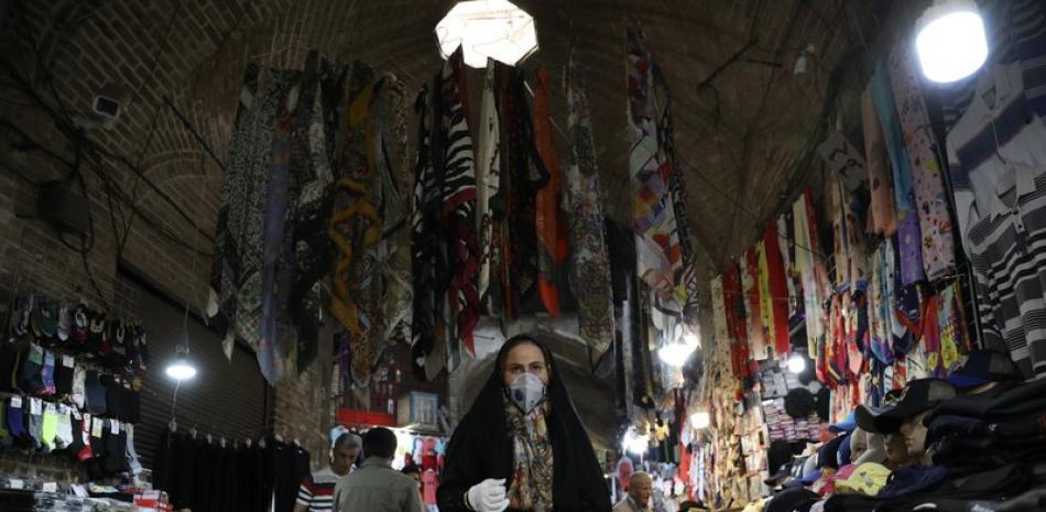 Una mujer con mascarilla y guantes para protegerse del coronavirus camina en el bazar tradicional Qazvin a unos 150 kilómetros (93 millas) del noroeste de Teherán, Irán. (AP Foto/Vahid Salemi)