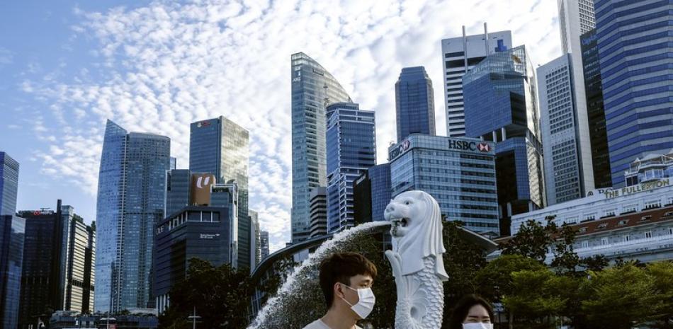 ARCHIVO - En esta imagen del 14 de marzo de 2020, una pareja con mascarillas pasea junto a la estatua del Merlion en Singapur. (AP Foto/Ee Ming Toh, Archivo)