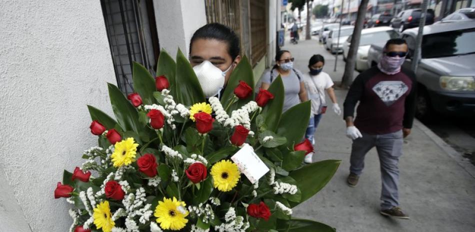 Leo Carbajal utiliza un cubrebocas el domingo 10 de mayo de 2020 mientras carga un arreglo floral para su madre Cynthia por el Día de las Madres en el mercado de flores de Los Ángeles. (AP Foto/Marcio José Sánchez)