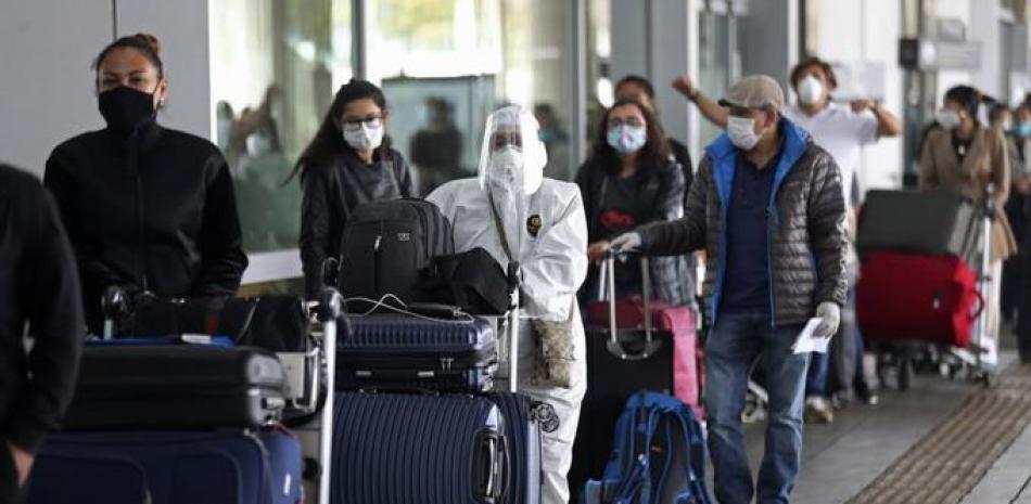 Pasajeros hacen fila para un vuelo humanitario a Italia el lunes 18 de mayo de 2020 usando mascarillas para protegerse del coronavirus, una pandemia que ha ocasionado la cancelación de vuelos nacionales e internacionales en el aeropuerto El Dorado en Bogotá, Colombia. (AP Foto/Fernando Vergara)