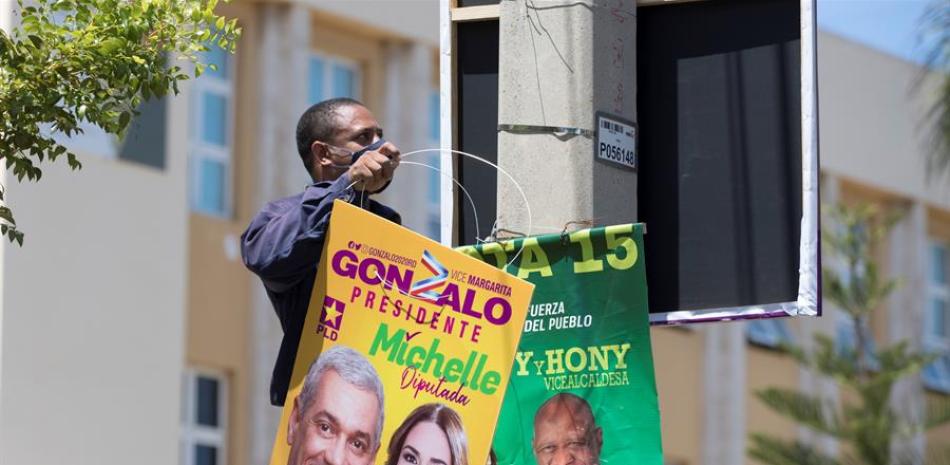 Un hombre cuelga un cartel de campaña política este viernes, en Santo Domingo (República Dominicana). El país ya está inmerso en la campaña electoral de cara a los comicios presidenciales y legislativos del próximo 5 de julio, sin dejar de mirar de reojo al comportamiento de la pandemia, que ya ha obligado a aplazar una vez esta cita con las urnas. EFE/ Orlando Barría