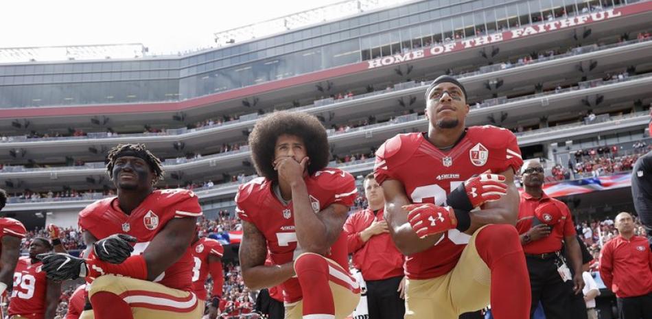 En esta foto del 2 de octubre de 2016, aparecen arrodillados, de izquierda a derecha, Eli Harold, Colin Kaepernick y Eric Reid, de los 49ers de San Francisco, durante la interpretación del Himno Nacional estadounidense. AP/Marcio José Sánchez.