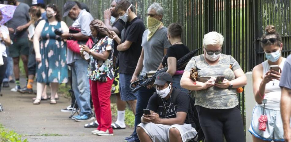 Steven Posey mira su celular mientras espera para votar, el martes 9 de junio de 2020 Central Park, Atlanta. Los votantes reportaron esperas de unas tres horas. (AP Foto/John Bazemore)