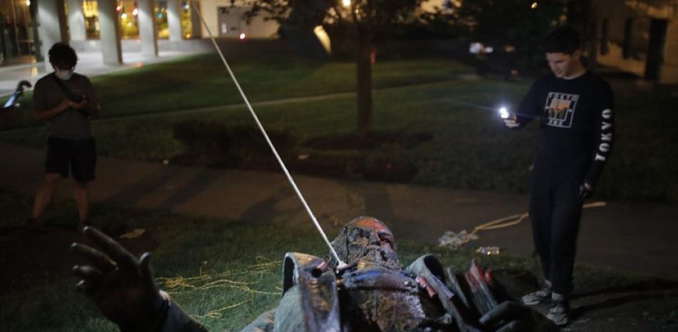 Un hombre usa su celular para grabar la estatua de Albert Pike, la única de un general del ejército confederado en la capital de Estados Unidos, después de que fue derribada por manifestantes e incendiada en Washington en las primeras horas del sábado 20 de junio de 2020. (AP Foto/Maya Alleruzzo)