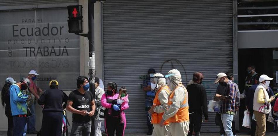 Trabajadores con treje de protección para prevenir el nuevo coronavirus caminan junto a peatones en Quito, Ecuador. /AP