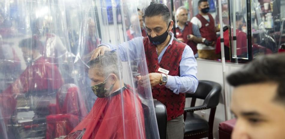 Peter Shamuelov, de pie al centro, porta una mascarilla mientras le corta el cabello a un cliente el lunes 22 de junio de 2020 en la peluquería Ace of Cuts, en Nueva York. (AP Foto/John Minchillo)