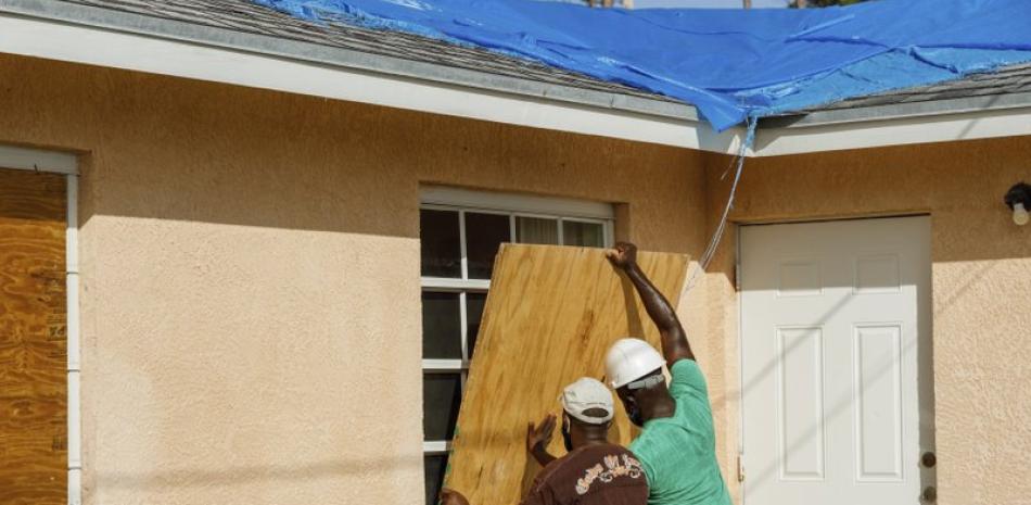 Residentes cubren una ventana con un tablón de madera antes de la llegada del huracán Isaías, en el vecindario de Heritage, en Freeport, en la isla de Gran Bahama, Bahamas, el 31 de julio de 2020. (AP Foto/Tim Aylen)