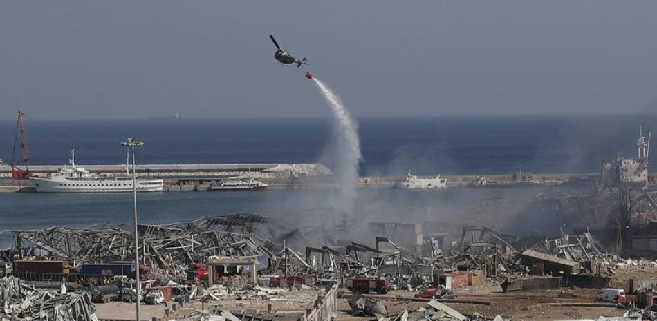 Un helicóptero del ejército libanés arroja agua sobre el sitio de una explosión en el puerto de Beirut ayer miércoles. La explosión del martes sacudió la capital, matando al menos a cien personas e hiriendo a miles. (AP Foto/Hussein Malla)