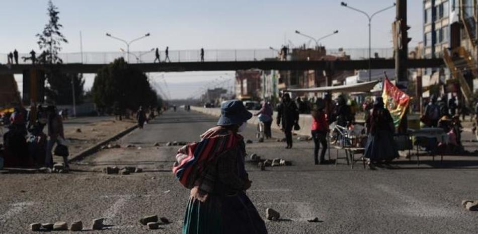 Una mujer que usa una mascarilla para prevenir el nuevo coronavirus camina por una calle bloqueada por manifestantes que protestan contra la postergación de las elecciones presidenciales en El Alto, Bolivia, el miércoles 5 de agosto de 2020. (AP Foto/Juan Karita)