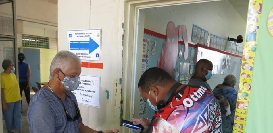 Un voluntario escanea las huellas dactilares de una persona antes de que emita su voto en Loíza, Puerto Rico, el domingo 16 de agosto de 2020. (AP Foto/Dánica Coto)