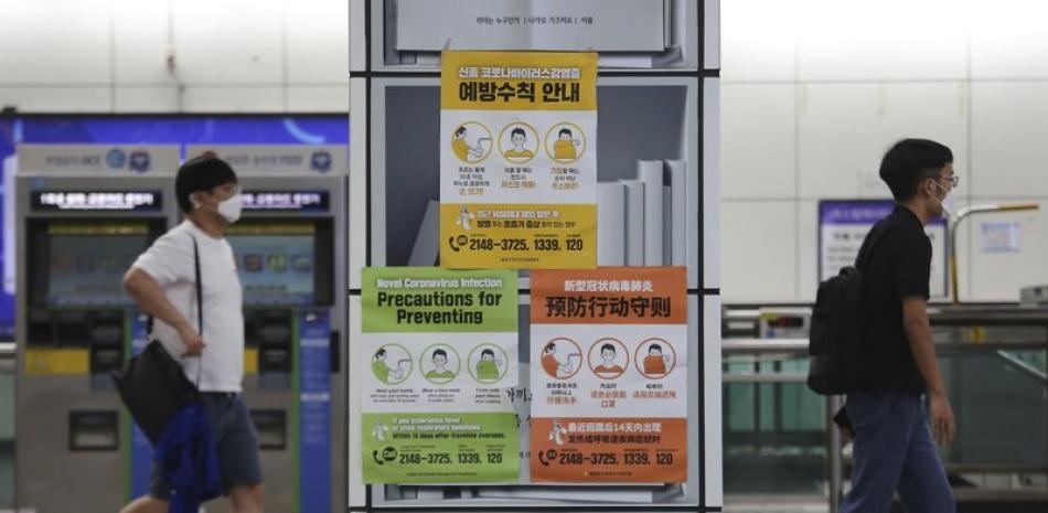 Dos personas, con mascarilla en plena pandemia del coronavirus, pasan junto a carteles que avisan sobre las precauciones a tomar durante la pandemia, en una estación de metro, en Seúl, Corea del Sur, el 18 de agosto de 2020. (AP Foto/Ahn Young-joon)