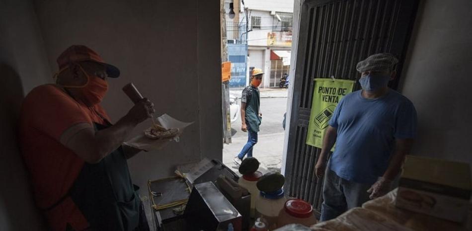 El vendedor de hamburguesas y perros calientes Pablo Emilio Buitrago hace una hamburguesa para un cliente en su puesto de comida dentro de la casa de su novia en el barrio San Agustín de Caracas, Venezuela. Foto: AP/Matias Delacroix.
