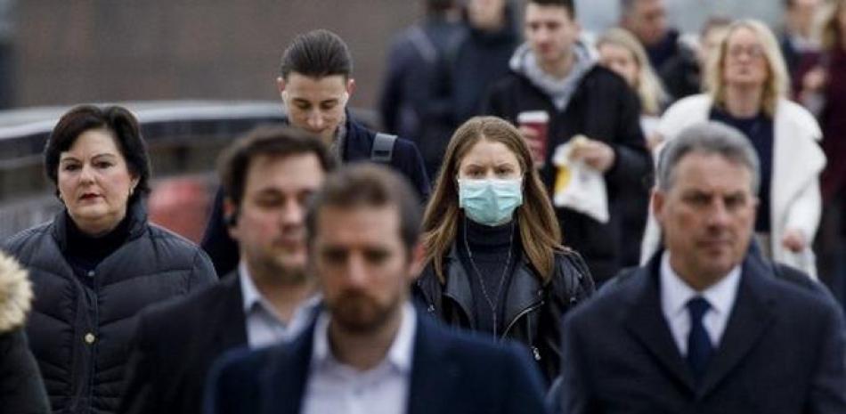 Personas caminado en un calle de Londres, donde se observa solo a una usando mascarilla. / AFP