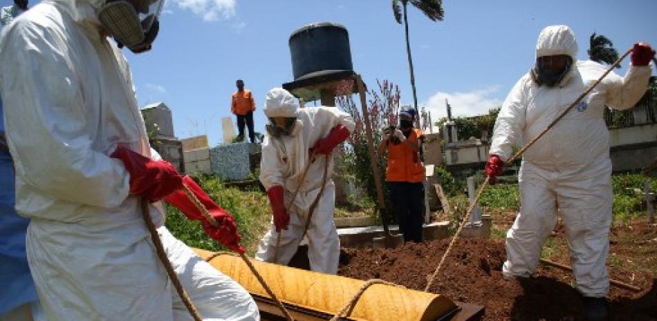 Miembros de Protección Civil con trajes de bioseguridad entierran el ataúd de una víctima del coronavirus COVID-19 en el cementerio Municipal de San Cristóbal, Venezuela. Fuente: Carlos Eduardo Ramírez/AFP.