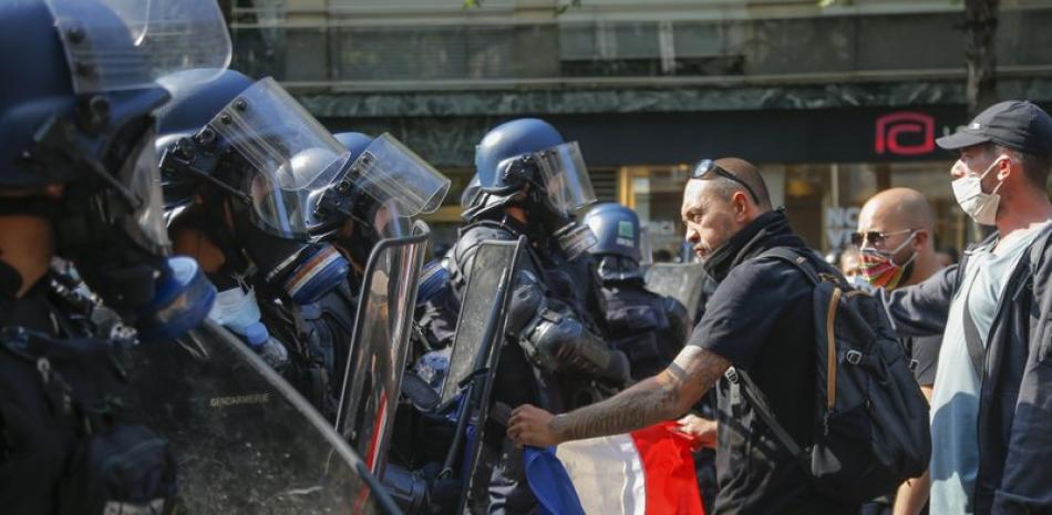 Un manifestante de los chalecos amarillos alza una bandera francesa frente a la policía antimotines durante una marcha en París. Foto: AP/Michel Euler.