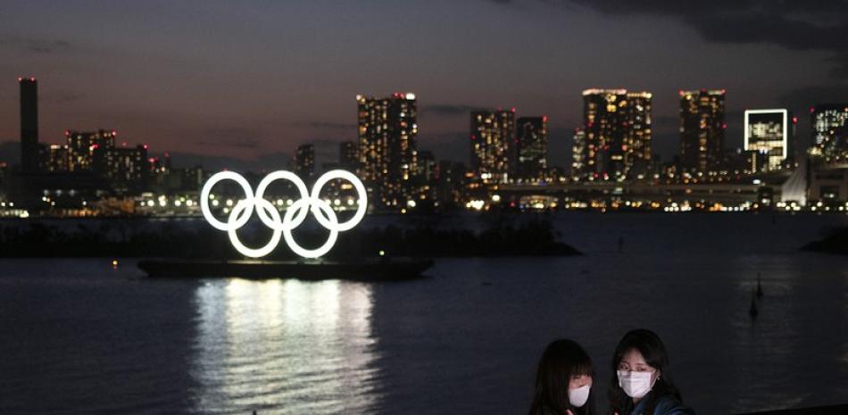 En esta fotografía del 12 de marzo de 2020, dos mujeres se toman una fotografía con los aros olímpicos en el fondo en Tokio.