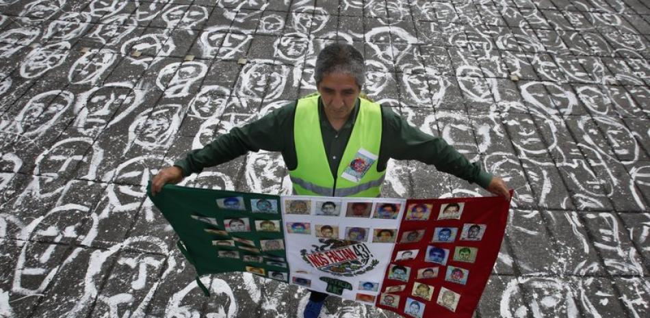 Un hombre que carga una bandera mexicana con retratos de los 43 estudiantes de la escuela normal rural de Ayotzinapa frente al monumento del Ángel de la Independencia en Ciudad de México. Foto: AP/Marco Ugarte.