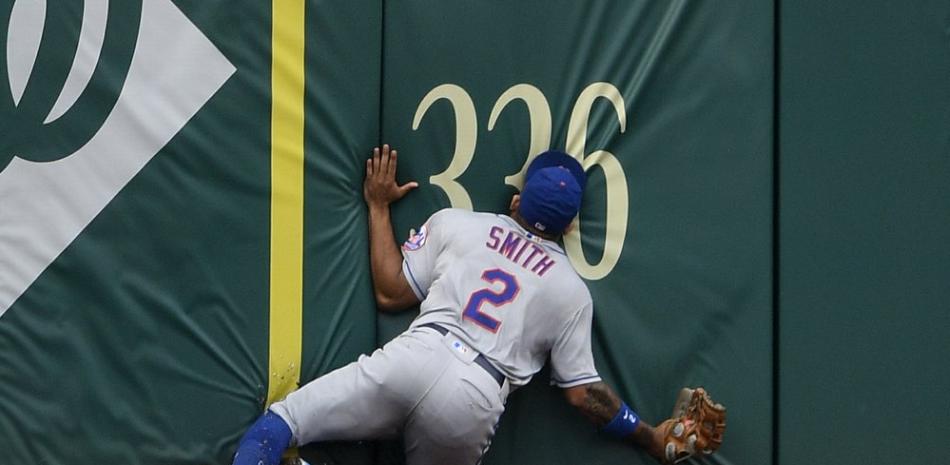 Dominic Smith de los Mets de Nueva York se estrella contra la pared del jardín mientras persigue un elevado que fue a por un jonrón dentro del parque de Andrew Stevenson de los Nacionales de Washington durante la quinta entrada del primer juego de béisbol de una doble cartelera.