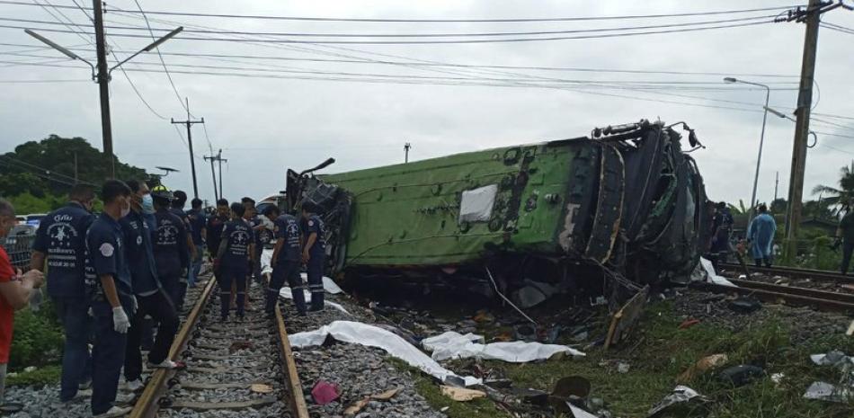Rescatistas junto a un vehículo dañado y varios cuerpos cubiertos de sábanas blancas, tras una colisión entre un autobús y un tren en la provincia de Chacheongsao, 80 kilómetros (50 millas) al este de Bangkok, Tailandia, el domingo 11 de octubre de 2020. (Daily News Via AP)