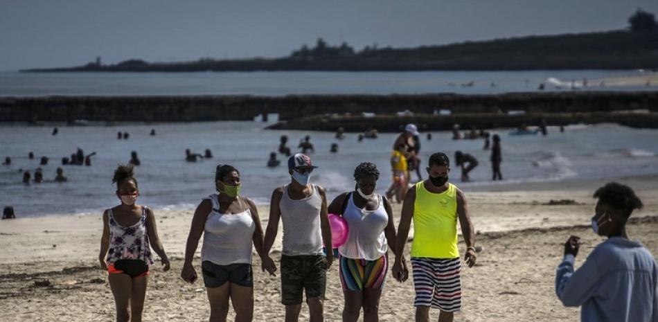 Personas usan máscaras como precaución contra la propagación del nuevo coronavirus caminan en la playa en La Habana. Foto: AP/Ramón Espinosa.